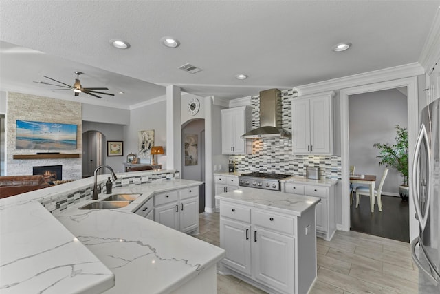 kitchen featuring appliances with stainless steel finishes, white cabinetry, sink, a center island, and wall chimney exhaust hood