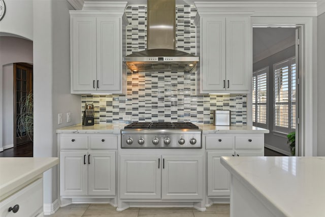 kitchen featuring stainless steel gas stovetop, white cabinetry, backsplash, light stone counters, and wall chimney exhaust hood