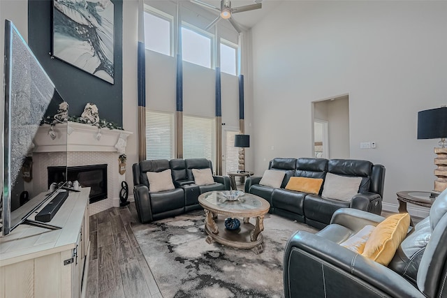 living room with dark wood-type flooring, a towering ceiling, a tiled fireplace, and ceiling fan