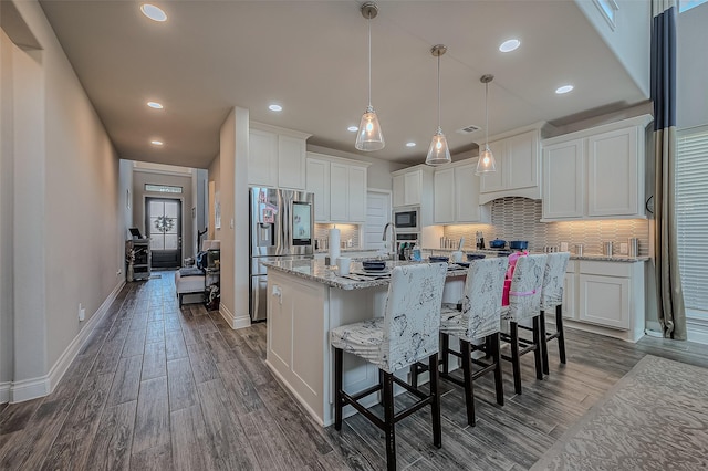 kitchen featuring white cabinetry, a center island with sink, stainless steel fridge, decorative light fixtures, and built in microwave