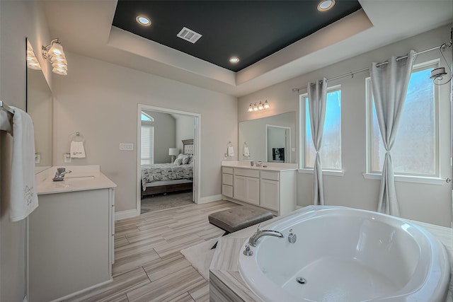 bathroom featuring a relaxing tiled tub, vanity, and a raised ceiling