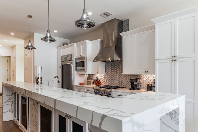 kitchen with pendant lighting, white cabinets, wall chimney exhaust hood, and built in appliances