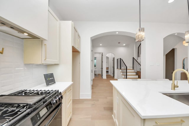 kitchen with stainless steel range with gas cooktop, tasteful backsplash, sink, hanging light fixtures, and a center island with sink