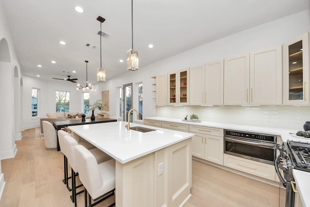 kitchen with sink, backsplash, hanging light fixtures, stainless steel appliances, and a center island with sink