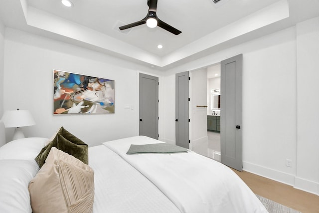 bedroom featuring a raised ceiling, connected bathroom, and ceiling fan