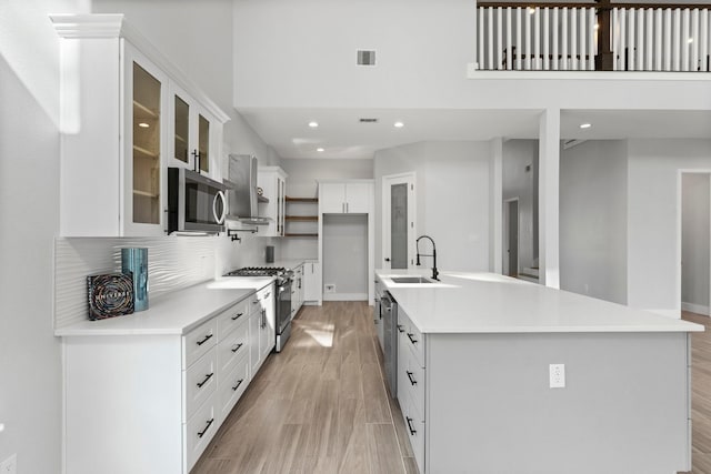 kitchen featuring sink, light wood-type flooring, a kitchen island with sink, appliances with stainless steel finishes, and white cabinets