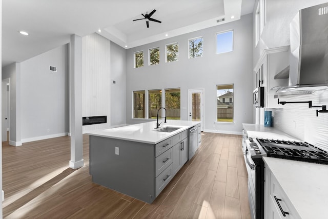 kitchen featuring appliances with stainless steel finishes, an island with sink, sink, ceiling fan, and gray cabinetry