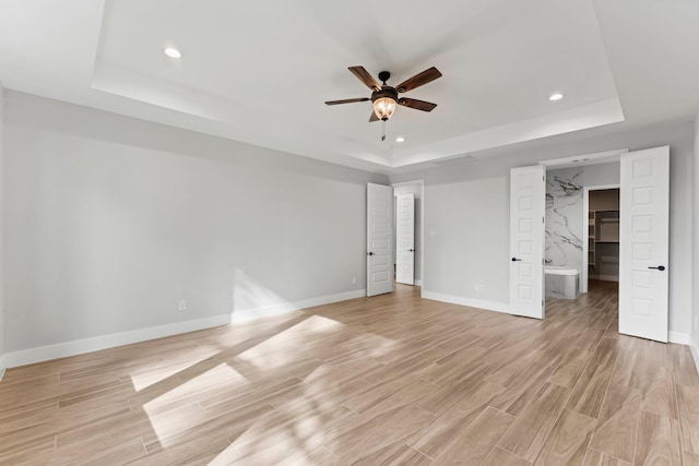 unfurnished bedroom with ceiling fan, ensuite bathroom, and a raised ceiling