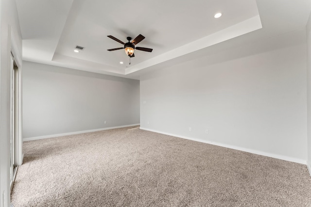 carpeted empty room with ceiling fan and a raised ceiling