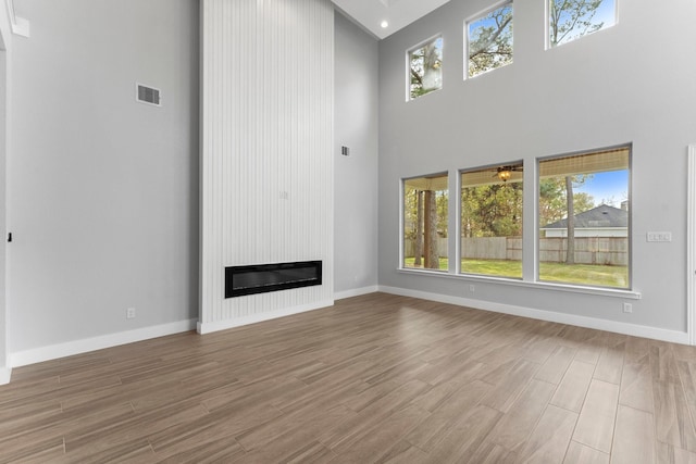 unfurnished living room with a large fireplace, a wealth of natural light, and a high ceiling