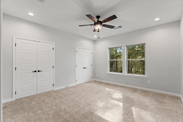 unfurnished bedroom with ceiling fan, carpet, and multiple closets