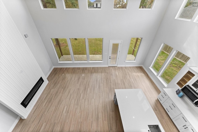 unfurnished living room featuring light hardwood / wood-style floors, a high ceiling, and a fireplace