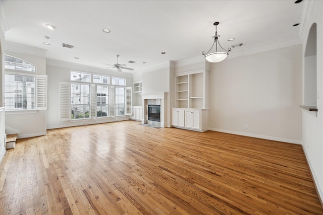 unfurnished living room with light wood-type flooring, ornamental molding, built in features, and a tile fireplace