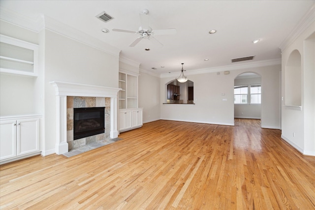 unfurnished living room with light hardwood / wood-style floors, ceiling fan, a tiled fireplace, built in features, and ornamental molding