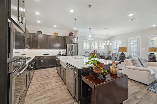 kitchen with appliances with stainless steel finishes, pendant lighting, dark brown cabinetry, light hardwood / wood-style floors, and a center island with sink