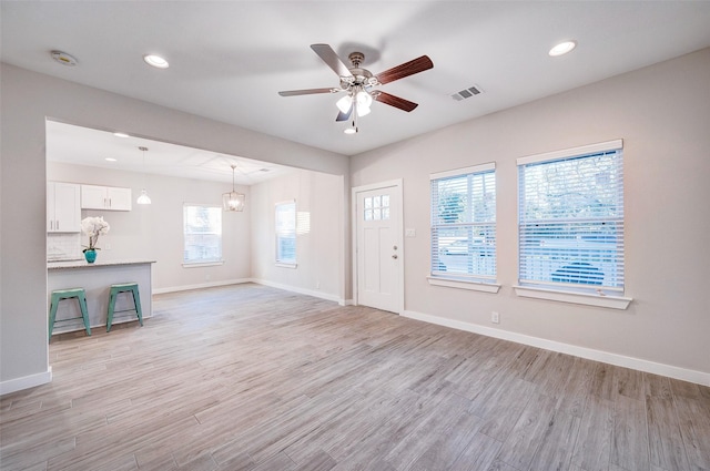 unfurnished living room featuring a healthy amount of sunlight, ceiling fan with notable chandelier, and light hardwood / wood-style flooring