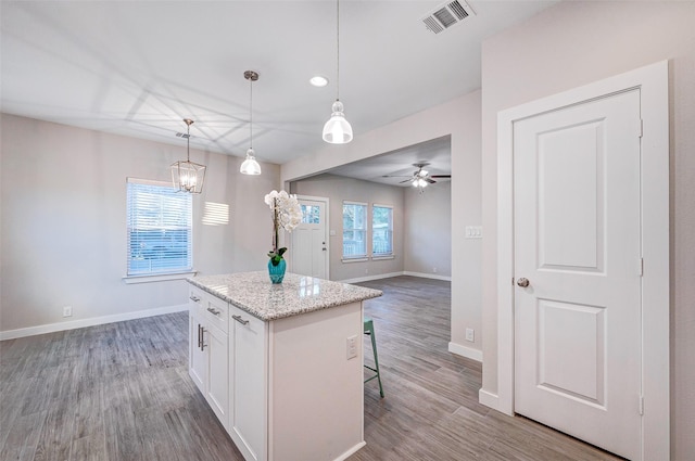 kitchen with a center island, a breakfast bar, white cabinetry, hanging light fixtures, and light stone countertops