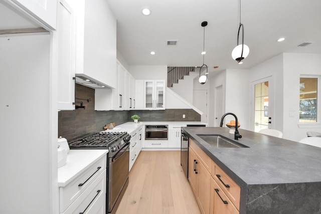 kitchen featuring white cabinetry, a kitchen island with sink, gas range, and sink