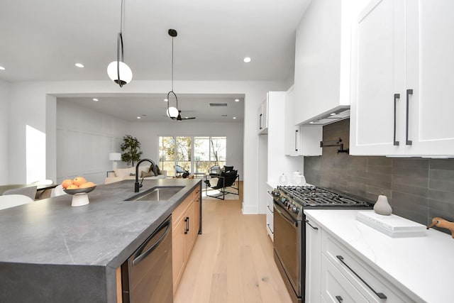 kitchen featuring decorative light fixtures, sink, white cabinets, a kitchen island with sink, and gas stove