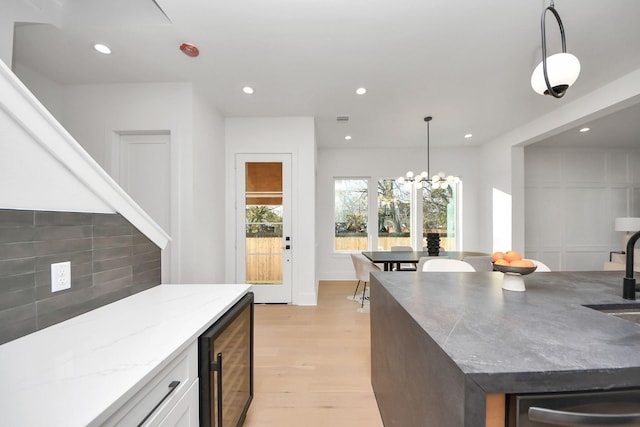 kitchen featuring pendant lighting, white cabinets, beverage cooler, light stone countertops, and an inviting chandelier