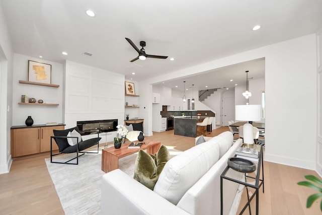 living room featuring sink, a large fireplace, ceiling fan, and light wood-type flooring