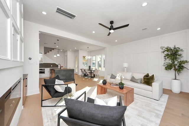 living room with sink, ceiling fan with notable chandelier, and light wood-type flooring