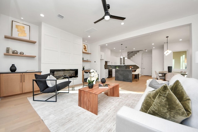 living room featuring a large fireplace, ceiling fan, and light wood-type flooring