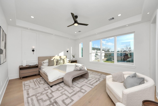 bedroom featuring ceiling fan, a tray ceiling, and light wood-type flooring