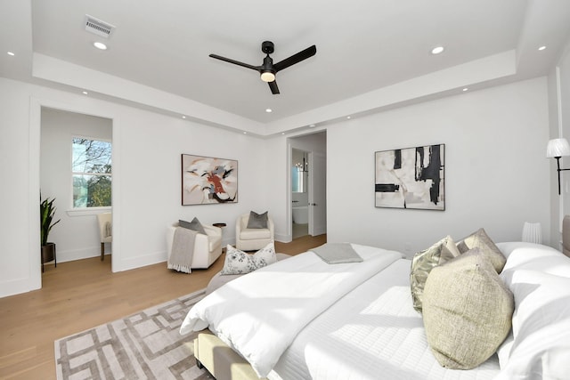 bedroom with ceiling fan, a tray ceiling, and light hardwood / wood-style flooring