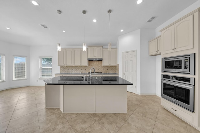 kitchen with stainless steel appliances, hanging light fixtures, a center island with sink, and cream cabinets