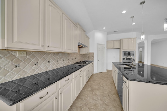 kitchen with dark stone counters, hanging light fixtures, a kitchen island with sink, sink, and stainless steel appliances