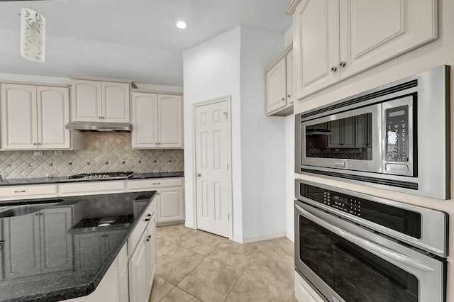 kitchen with appliances with stainless steel finishes, cream cabinetry, tasteful backsplash, dark stone counters, and light tile patterned floors