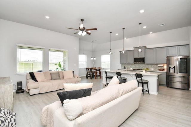 living room with light wood-type flooring, ceiling fan, and sink