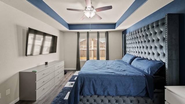 bedroom with light wood-type flooring, ceiling fan, and a tray ceiling