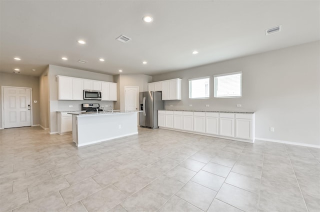 kitchen with light tile patterned floors, white cabinets, stainless steel appliances, and an island with sink