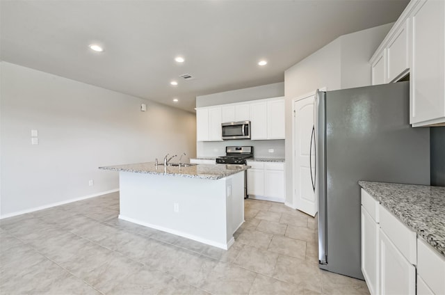 kitchen featuring stainless steel appliances, a kitchen island with sink, white cabinets, and light stone countertops