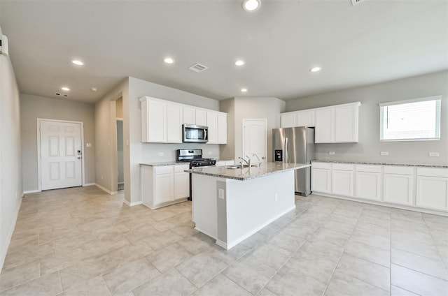 kitchen with sink, white cabinetry, a kitchen island with sink, stainless steel appliances, and light stone counters