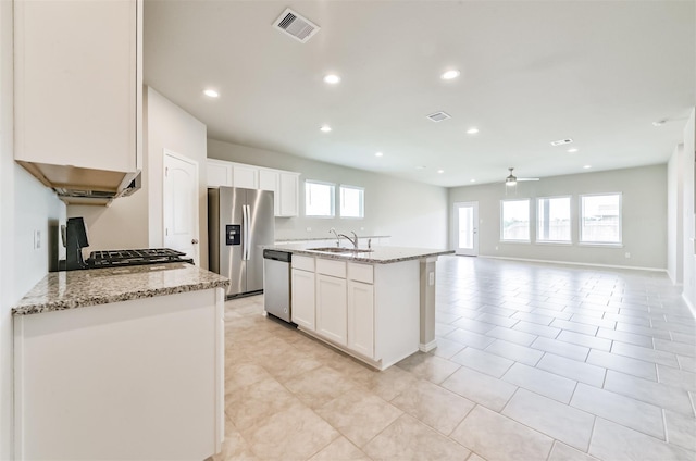 kitchen featuring a center island with sink, sink, light stone countertops, appliances with stainless steel finishes, and white cabinets