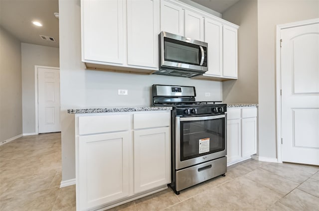 kitchen featuring light tile patterned floors, white cabinets, light stone counters, and appliances with stainless steel finishes