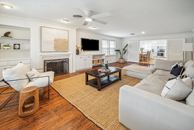 living room featuring crown molding, ceiling fan, built in shelves, and light wood-type flooring