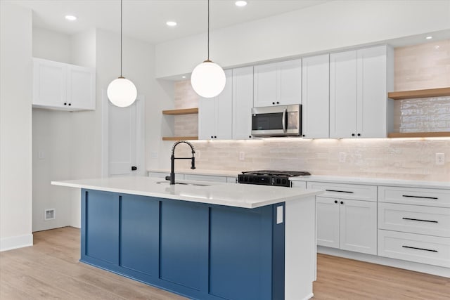 kitchen with hanging light fixtures, white cabinets, a kitchen island with sink, and range