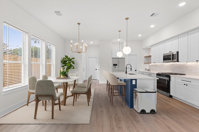 kitchen featuring light hardwood / wood-style flooring, hanging light fixtures, appliances with stainless steel finishes, an island with sink, and white cabinets