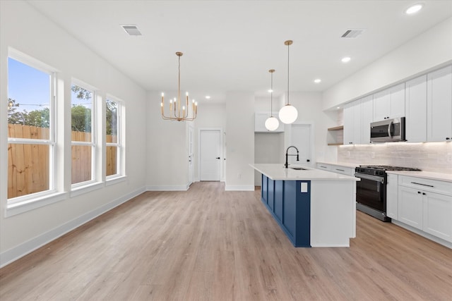 kitchen featuring an inviting chandelier, hanging light fixtures, an island with sink, white cabinets, and range with gas stovetop