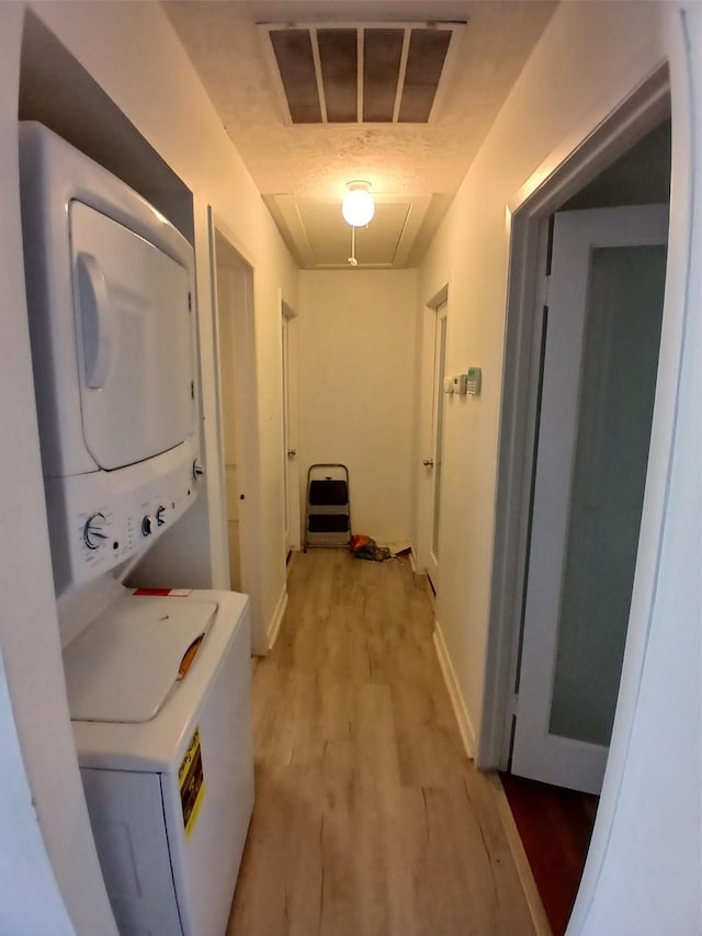 washroom with stacked washing maching and dryer and light hardwood / wood-style flooring