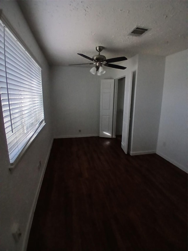 empty room with ceiling fan, a textured ceiling, and dark hardwood / wood-style floors