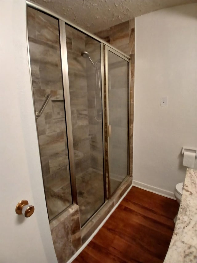 bathroom featuring a shower with shower door, hardwood / wood-style floors, and toilet