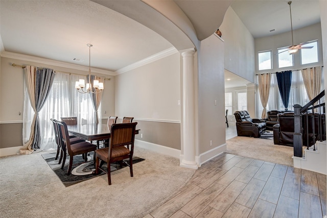 carpeted dining space with ceiling fan with notable chandelier, decorative columns, and crown molding