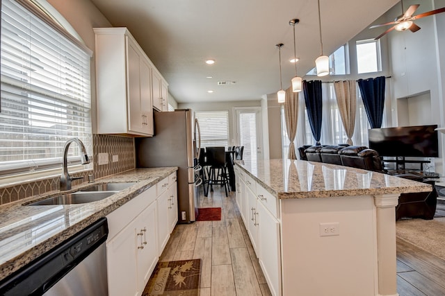 kitchen with stainless steel appliances, white cabinets, a kitchen island, light stone counters, and sink