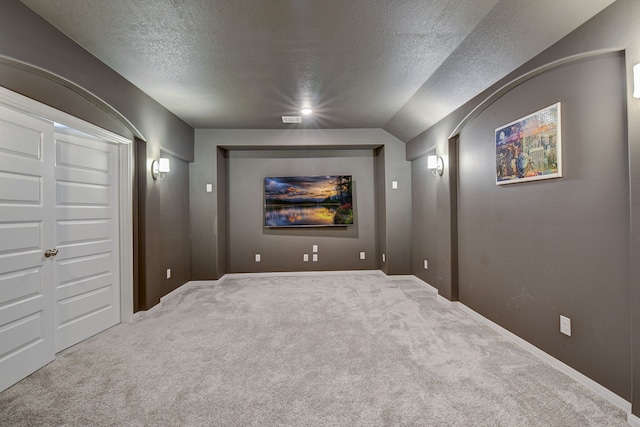 carpeted home theater room featuring lofted ceiling and a textured ceiling