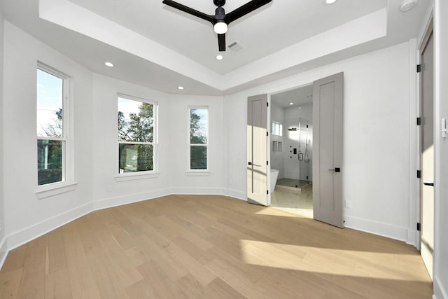 unfurnished bedroom with ceiling fan, light hardwood / wood-style flooring, a tray ceiling, and multiple windows